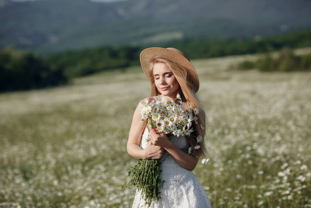 beautiful young woman in a camomile field in a picturesque valley. happy young lady and spring green nature, harmony concept. the idea of self-care, a healthy lifestyle and a positive attitude - Valokuva, kuva