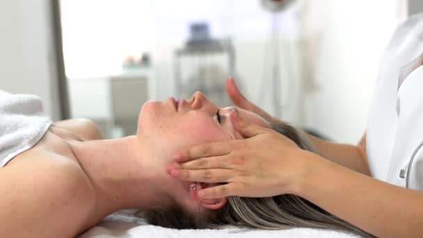 Mujer rubia joven recibiendo un masaje en la cabeza en un centro de spa
. - Metraje, vídeo