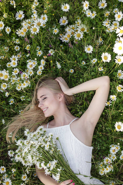 beautiful young woman in a camomile field in a picturesque valley. the idea of self-care, a healthy lifestyle and a positive attitude. concept of healthy snow-white smile and healthy skin and hair - Photo, Image