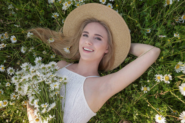beautiful young woman in a camomile field in a picturesque valley. the idea of self-care, a healthy lifestyle and a positive attitude. concept of healthy snow-white smile and healthy skin and hair - Photo, image