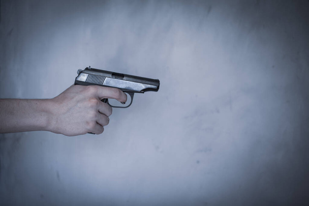 Mann hält Waffe - Aggression. Große Pistole in der Hand, auf grauem Hintergrund, getönt - Foto, Bild