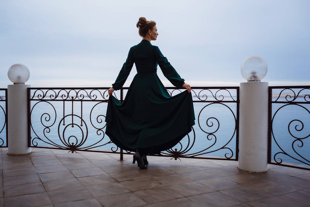 Krásná mladá žena čeká na akci v restauraci na terase. Příprava na slavnosti a události. Luxusní šaty s výhledem na moře - Fotografie, Obrázek