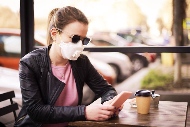Shot of young woman wearing a respirator mask device for health protection during the coronavirus outbreak. Confident woman text messaging while on the street. - Φωτογραφία, εικόνα