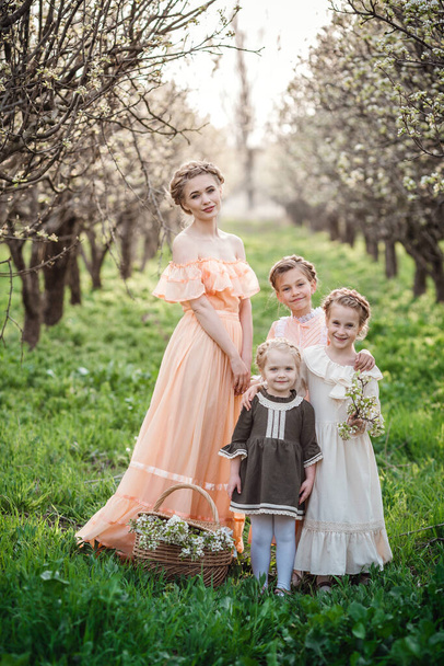 Güzel kızlar ve ablaları çiçeklerle dolu bahçede yürüyüş yapıyorlar. Arkadaş canlısı bir aile ve mutlu bir çocukluk fikri. Retro elbiseler - Fotoğraf, Görsel