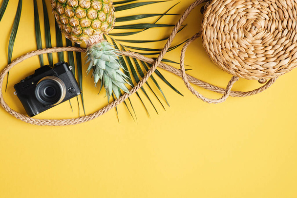 Flat lay traveler accessories on yellow background. Frame border made of palm leaf, rattan straw bag, vintage camera, pineapple. Top view travel or vacation concept. Summer background - Photo, image