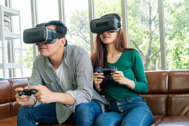 Junges glückliches asiatisches Paar spielt Videospiele im Wohnzimmer. Fröhliche Menschen haben Spaß am Computerspielkonzept. - Foto, Bild