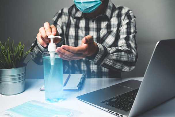Coronavirus disease or COVID-19 protection concept - Young man work in office room at home with protective and cleaning equipment to protect against corona virus while using laptop computer at desk. - Фото, изображение