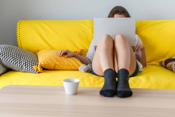 Woman freelancer sitting on the couch with laptops in the socks and putting legs on the table. Work at home. Concept. Cup coffee. Relax at home. - Photo, Image