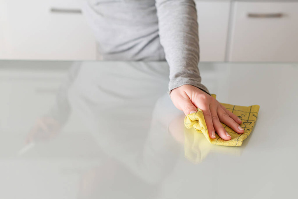 Cleaning wipe with a cloth in the hands of woman kitchen table.  Housekeeping service. The concept of disinfection. Protection from viruses and bacteria - Fotoğraf, Görsel
