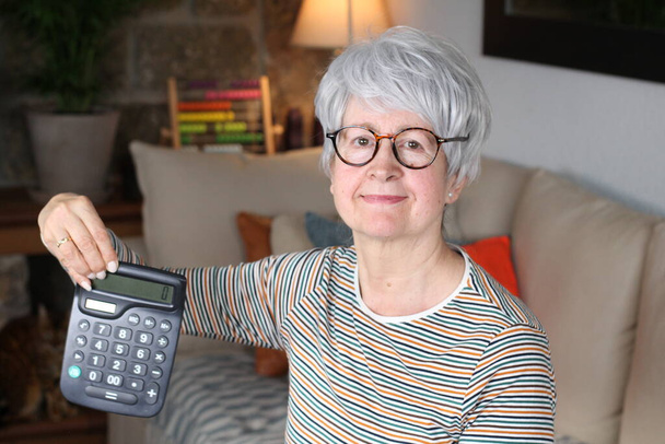 Беспокойная пожилая женщина держит калькулятор
 - Фото, изображение