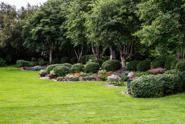 Un diseño de paisaje de jardín con césped, árboles, arbustos topiarios de hoja perenne y macizo de flores
 - Foto, Imagen