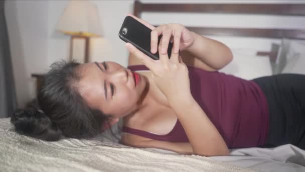 young beautiful and happy Asian korean woman using mobile phone social media texting with her boyfriend or enjoying online dating app smiling cheerful lying on bed at home  - 映像、動画