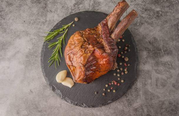 Smoked meat rack on a black round slate with spices, rosemary, top view - Fotó, kép