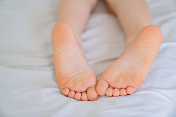Patas de niño en la cama. pies rosados y tacones lisos
 - Foto, Imagen