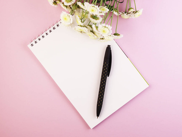 an empty Notepad with a pen and a flower bouquet on a pastel pink background. white notebook with daisies on a purple background - Foto, Imagem