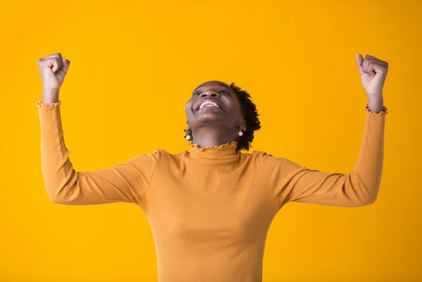 beautiful young african woman on yellow background with hands up - Photo, Image
