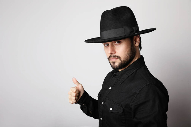 Side portrait of bearded hipster wearing black fedora hat and shirt looking at camera. - Foto, Imagem