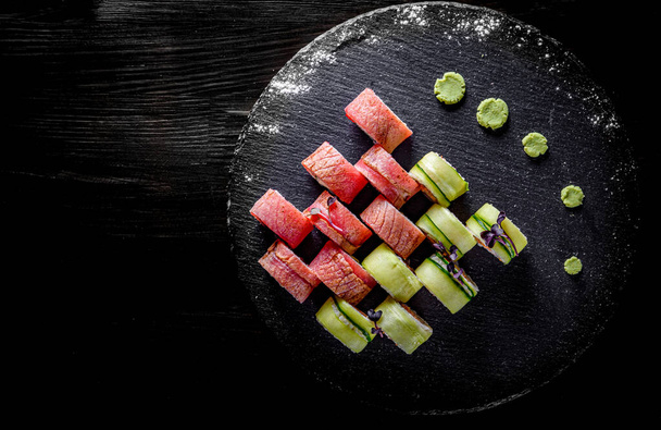 juego de rollos de sushi con atún, aguacate, queso crema, pepino, arroz en plato sobre fondo de mesa de madera negra
 - Foto, imagen