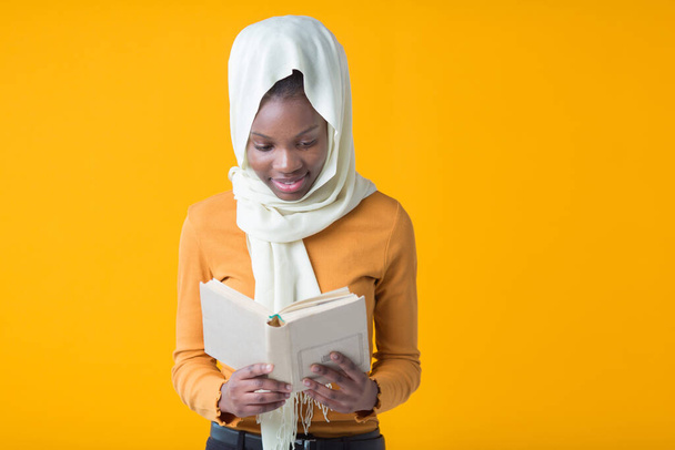 beautiful young african woman on a yellow background with a muslim shawl with a book in her hands - Fotoğraf, Görsel