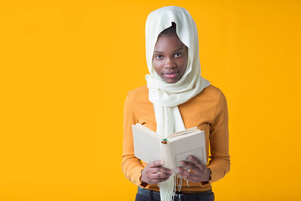 beautiful young african woman on a yellow background with a muslim shawl with a book in her hands - Foto, immagini