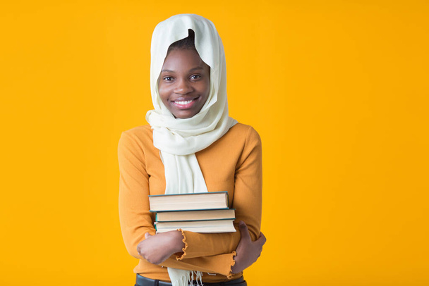 beautiful young african woman on a yellow background with a muslim shawl with books in her hands - Foto, Imagen
