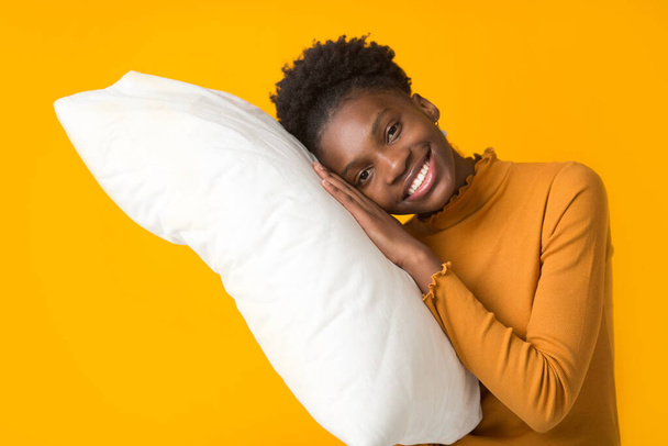 beautiful young african woman on a yellow background with a pillow - Foto, imagen