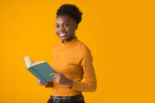 beautiful young african woman on yellow background with a book - Foto, Imagem