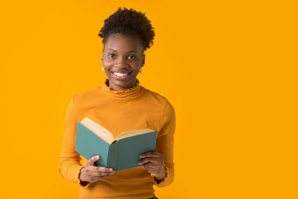 beautiful young african woman on yellow background with a book - Fotó, kép