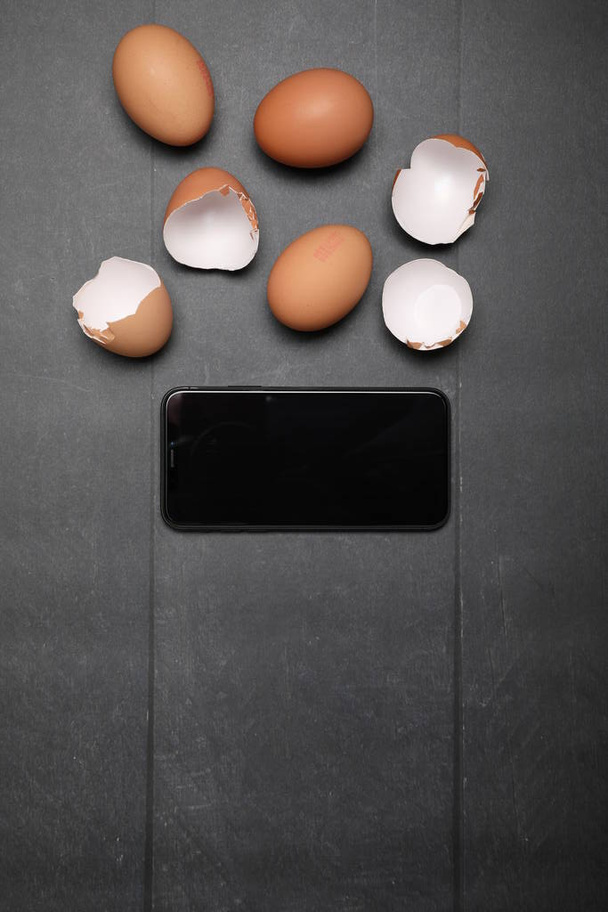 Raw chicken eggs and black smartphone on wooden table. Space for text. - Fotó, kép