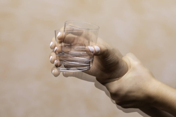 Closeup view on the shaking hand of a person holding drinking glass suffering from Parkinson's disease - Photo, Image