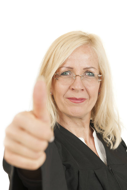 Frontalansicht einer blonden Frau mittleren Alters in Richterrobe, die die Daumen nach oben zeigt und vor weißem Hintergrund in die Kamera lächelt. - Foto, Bild