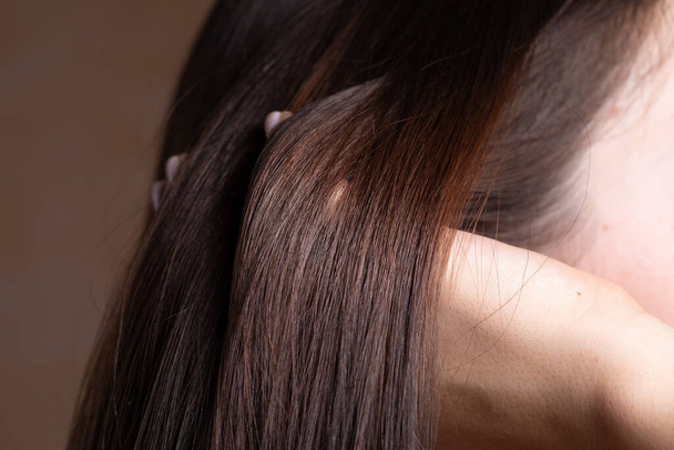 Detail eines brünetten Mädchens, das ihre Haare mit den Fingern entwirrt - Foto, Bild