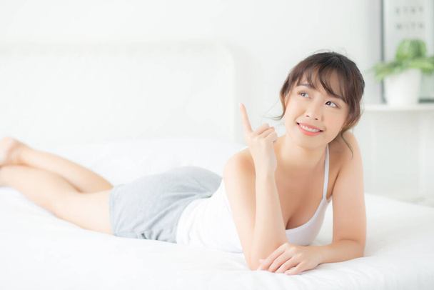 Portrét krásná mladá asijská žena úsměv probudit zdravé a wellness v dopoledních hodinách, krása asijské dívka ležící a ukazující něco péče o pleť a make-up kosmetické s šťastný, životní styl a relaxační koncept. - Fotografie, Obrázek