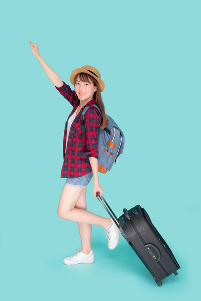 Красива молода азіатка тягне валізу ізольовано на синьому фоні, азіатська дівчина, яка має вираз, весела тримає багаж, що йде у відпустку з збудженою концепцією подорожі та подорожей
. - Фото, зображення