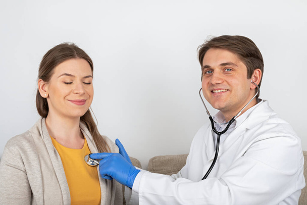 Young male doctor consulting female patient with influenza symptoms at home - Photo, Image