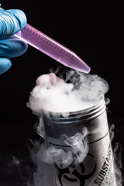 A closeup view of a laboratory technician carrying out a science experiment with purple liquid over freezing nitrogen. Steam rises from metal bucket. - Фото, изображение