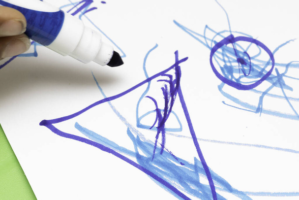 Nahaufnahme eines Kindes, das bunte Bilder mit einem blauen Filzstift auf weißem Papier zeichnet, vorschulische Kunst und Bildung, Lernen und Entwicklung von Säuglingen. - Foto, Bild