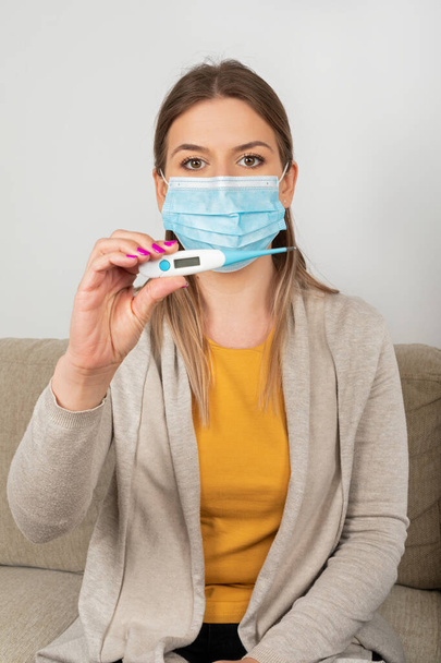 Young woman with coronavirus symptoms is at home wearing mask, holding thermometer  - self quarantine - Foto, Bild