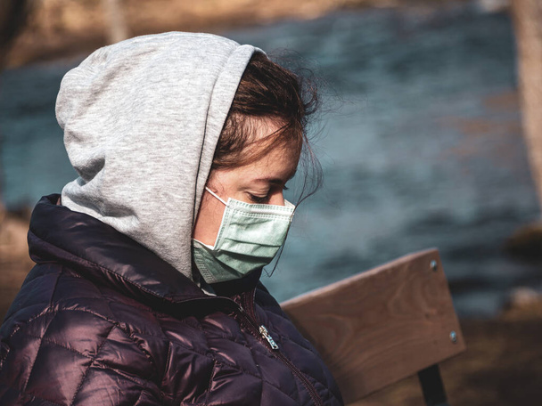 Θλιβερή γυναίκα που κάθεται μόνη στο παγκάκι φορώντας μάσκα προσώπου για να αποφύγει τη μόλυνση. Ο ιός Corona, ή Covid 19, εξαπλώνεται σε όλο τον κόσμο..  - Φωτογραφία, εικόνα