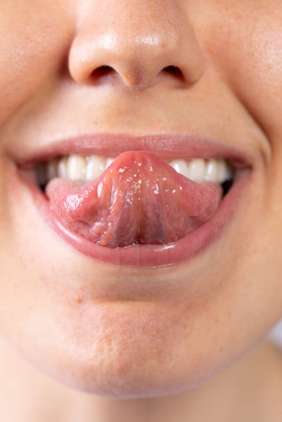 Közelkép egy gyönyörű kaukázusi lány szájáról. Kinyújtja a nyelvét, és az orra felé görbíti.. - Fotó, kép