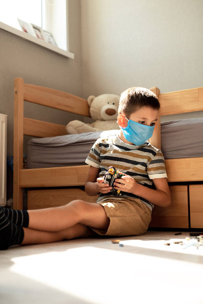 Stay at home quarantine coronavirus pandemic prevention. A boy in a protective medical mask plays and folds the constructor himself in his room. Prevention epidemic. COVID-19. - Foto, Imagem