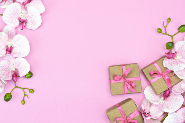flat-lay of present gift boxes with pink ribbon on pink background with orchid flowers. spring concept. Copy space - Foto, imagen