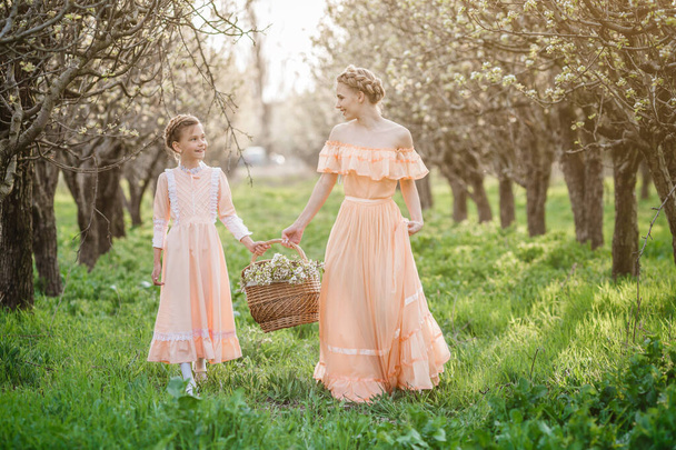 Two little sisters, younger and older, are walking in the garden, enjoying the spring in beautiful vintage dresses. The idea and concept of a friendly family and a happy childhood. - Foto, afbeelding