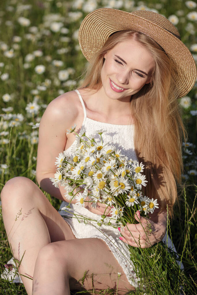beautiful young woman in a camomile field in a picturesque valley. happy young lady and spring green nature, harmony concept. the idea of self-care, a healthy lifestyle and a positive attitude - Photo, Image