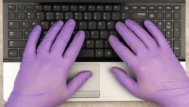 hands in medical gloves on the keyboard. Learning or working online in period of quarantine COVID-19.  - 写真・画像