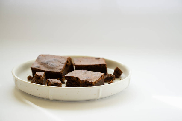 Morceaux carrés de brownie empilés dans une assiette blanche sur un fond blanc propre. Délicieux petit déjeuner au chocolat. Espace de copie. - Photo, image