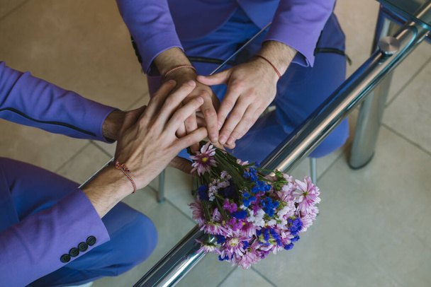 Hands of to partners homosexual couple on wedding day. Wedding bouquet of purple flowers on the table - Φωτογραφία, εικόνα