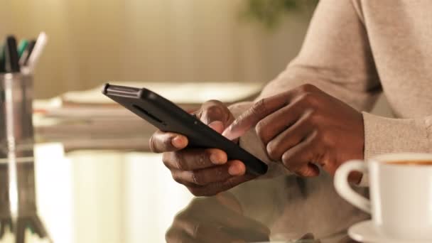 Close up of a black man hands texting on smart phone on a desk at home - Filmati, video