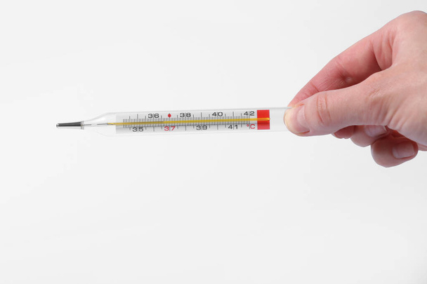 Thermometer in a woman hand isolated on white background. Temperature measuring by a thermometer. Fever measuring. selective focus. - Zdjęcie, obraz