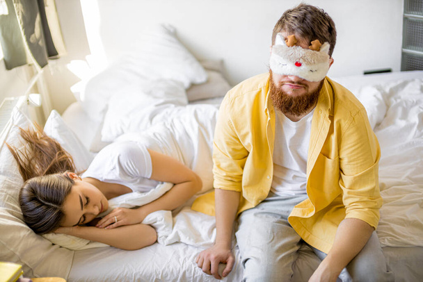 sleepy man in mask sit on bed near sleeping wife - Zdjęcie, obraz